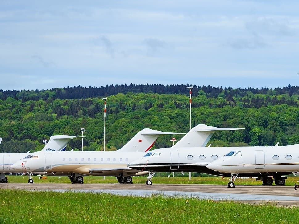 Professional pilot in uniform standing next to business jet at sunset
